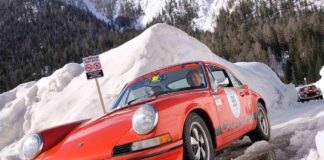A classic orange Porsche car driving through a snowy landscape during a winter rally
