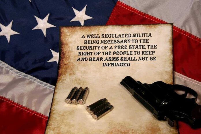 A revolver and bullets placed on an aged document with the Second Amendment text, set against an American flag background