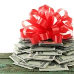 A stack of cash topped with a red ribbon bow