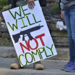 Protest sign reads: We Will Not Comply.