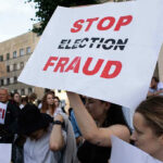 FBI SEIZES 700 Boxes From Georgia Election Warehouse People holding Stop Election Fraud protest signs.