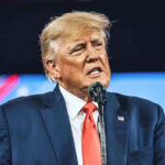 Trump UNLEASHES Davos Bombshell Man in suit speaking at a podium.