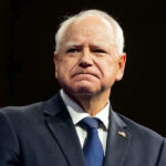 Trump Targets Walz Over Fraud Epidemic Man in suit with a U.S. flag pin.