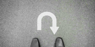 Feet in black shoes facing U-turn road marking.