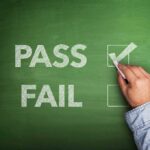 A hand marking a check in the PASS box on a chalkboard