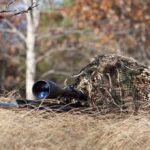 A sniper rifle partially covered in camouflage netting in a grassy area
