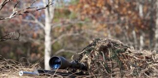 A sniper rifle partially covered in camouflage netting in a grassy area