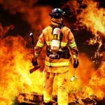 Fire Hides Pregnant Mom’s Grisly Home Murder Firefighter standing in front of a large fire, equipped with tools