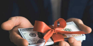 Hands holding stack of hundred-dollar bills with ribbon.