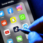 TikTok Bails, Big Tech Cornered Social media apps on phone screen with hand holding stylus.