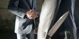 Two men shaking hands, one holding hidden knife.