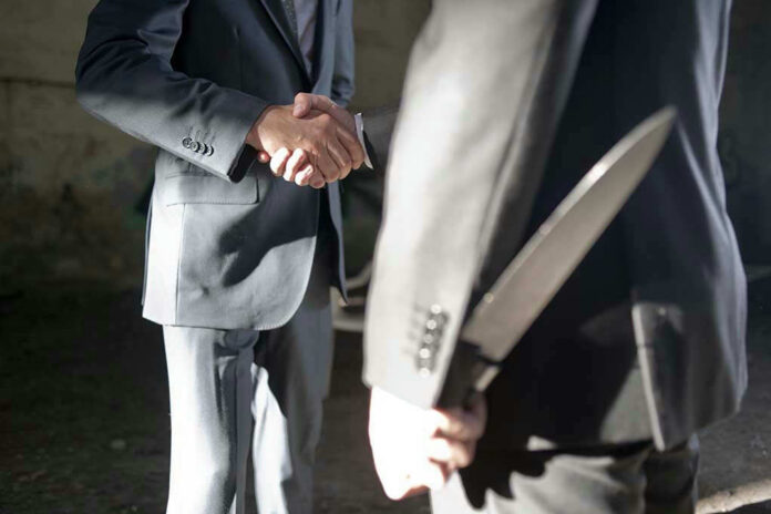 Two men shaking hands, one holding hidden knife.