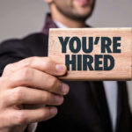Person holding a Youre Hired sign.