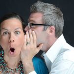 A surprised woman reacting while a man whispers in her ear