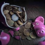 A broken pink piggy bank with coins spilling out onto a wooden surface