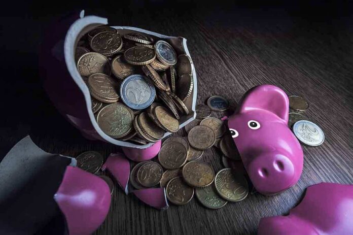 shutterstock_147048368.jpg A broken pink piggy bank with coins spilling out onto a wooden surface