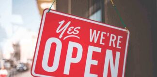 A red sign that reads Yes, We're Open hanging on a door