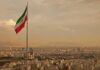 Iranian flag waving over a city skyline with mountains in the background