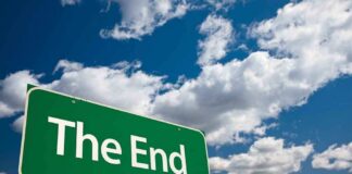 A green road sign displaying the words The End against a cloudy sky