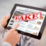 Person holding a tablet displaying a news website with a 'FAKE' stamp