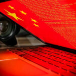 China Spy Bust Shakes UK’s TOP Politics Laptop screen displaying Chinese flag and code.