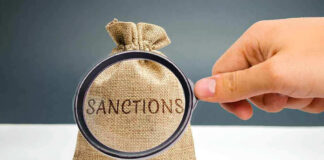 Hand holding magnifying glass over sack labeled Sanctions.
