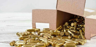 Box of brass bullets spilled on wooden surface.