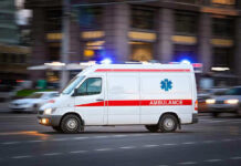 Ambulance driving on urban street with lights flashing.