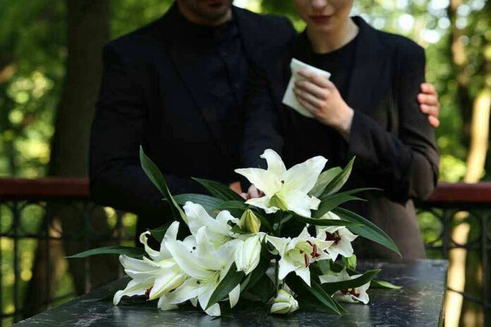 Mourners in black holding white flowers at funeral.