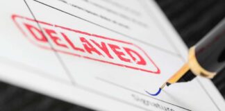 Close-up of a document with a DELAYED stamp and a pen about to sign