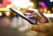 Mom MURDERED — Killer’s Horrifying Text A persons hand using a smartphone in a city at night with blurred lights in the background