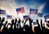 Silhouetted crowd holding American flags against a sunset sky