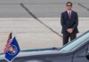 A security officer in a suit stands guard near a presidential vehicle at an airport