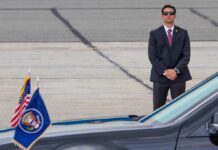 A security officer in a suit stands guard near a presidential vehicle at an airport