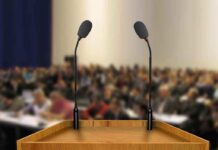 A wooden podium with two microphones in front of a blurred audience