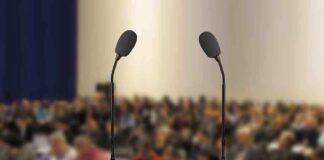 A wooden podium with two microphones in front of a blurred audience