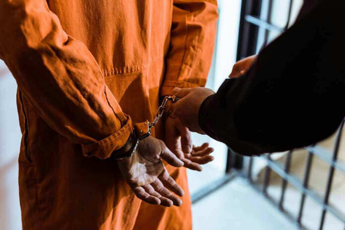 1036220185 Handcuffed person in orange jumpsuit being escorted.