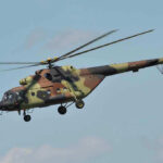 Camouflage military helicopter in flight against blue sky.