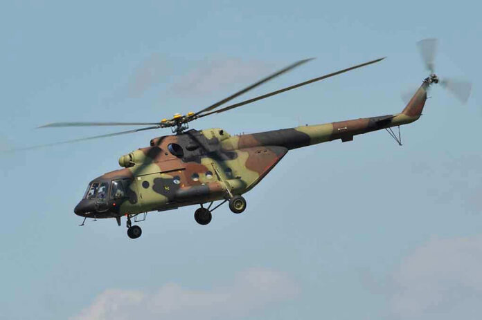 Camouflage military helicopter in flight against blue sky.