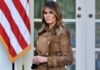 Woman in brown coat beside American flag.