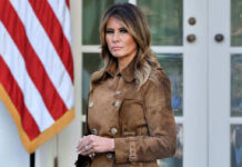 Woman in brown coat beside American flag.