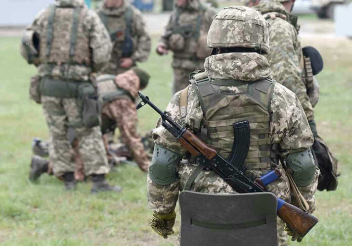2057061182 Soldiers in camouflage gear gathered on grass field.