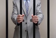 Businessman in a suit holding prison bars with handcuffs on his wrists