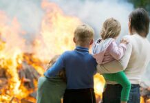 A family watching a large fire outdoors with children in their arms