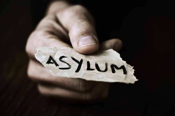 A hand holding a torn piece of paper with the word ASYLUM written on it