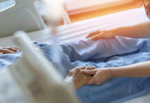 Hospital patient holding visitors hand reassuringly.