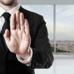 Person in suit with hand raised in stop gesture.