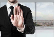 Person in suit with hand raised in stop gesture.
