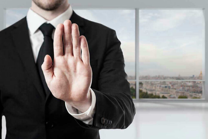 Person in suit with hand raised in stop gesture.