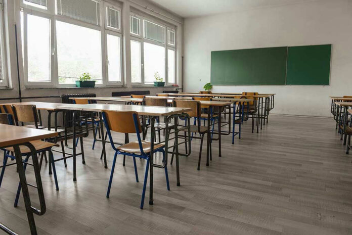 Empty classroom with desks, chairs, windows, and chalkboard.